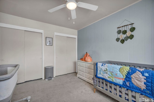 bedroom with multiple closets, light colored carpet, ornamental molding, and ceiling fan