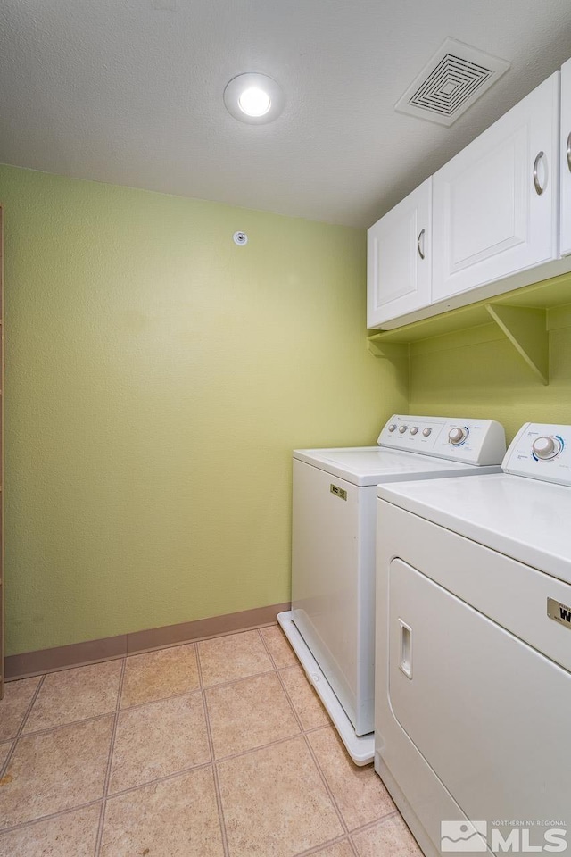 clothes washing area with cabinets, washer and dryer, and light tile patterned floors