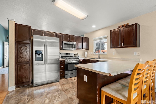 kitchen with a breakfast bar, sink, dark brown cabinetry, kitchen peninsula, and stainless steel appliances