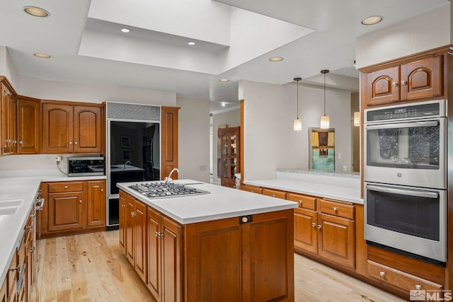 kitchen with stainless steel appliances, a kitchen island with sink, pendant lighting, and light hardwood / wood-style floors