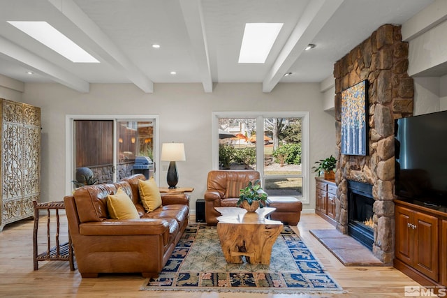 living room with a fireplace, a skylight, beam ceiling, and light wood-type flooring