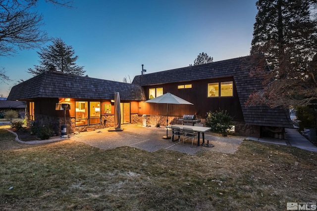 back house at dusk with a yard and a patio