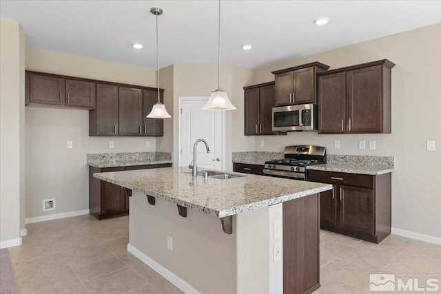 kitchen with sink, hanging light fixtures, stainless steel appliances, light stone counters, and a center island with sink