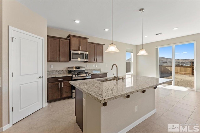 kitchen with pendant lighting, an island with sink, sink, stainless steel appliances, and light stone countertops