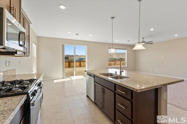 kitchen featuring pendant lighting, sink, stainless steel appliances, light stone countertops, and a center island with sink