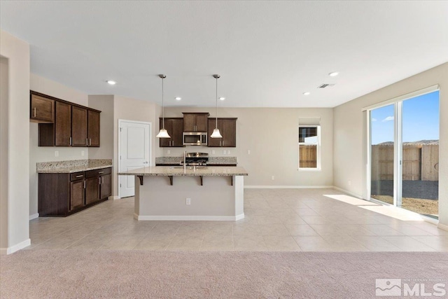 kitchen with pendant lighting, light stone counters, light colored carpet, and an island with sink