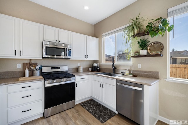 kitchen with white cabinetry, sink, light hardwood / wood-style floors, and appliances with stainless steel finishes