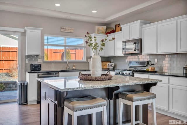 kitchen with sink, white cabinetry, a center island, appliances with stainless steel finishes, and dark stone counters