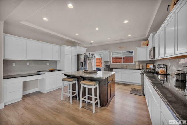 kitchen featuring sink, a center island, dark stone counters, stainless steel appliances, and white cabinets