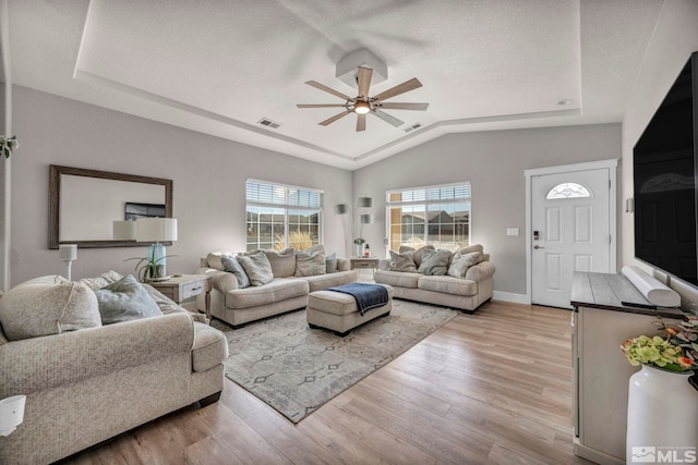 living room featuring lofted ceiling, a textured ceiling, a tray ceiling, ceiling fan, and light hardwood / wood-style floors