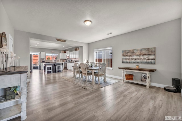 dining space with a healthy amount of sunlight, light hardwood / wood-style floors, and a textured ceiling