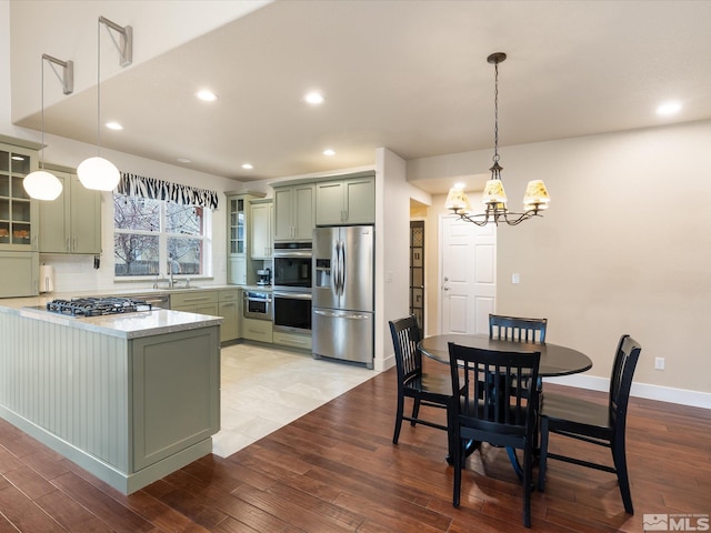 kitchen featuring stainless steel appliances, green cabinets, kitchen peninsula, and decorative light fixtures