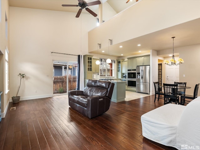 living room featuring a high ceiling, ceiling fan with notable chandelier, sink, and hardwood / wood-style floors