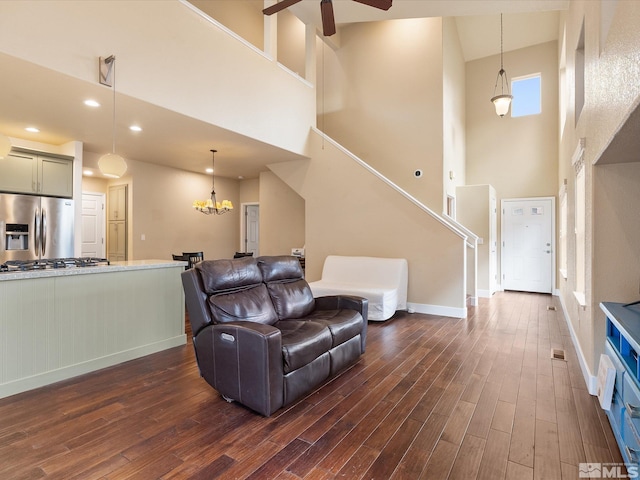 living room featuring ceiling fan with notable chandelier, dark wood-type flooring, and a towering ceiling