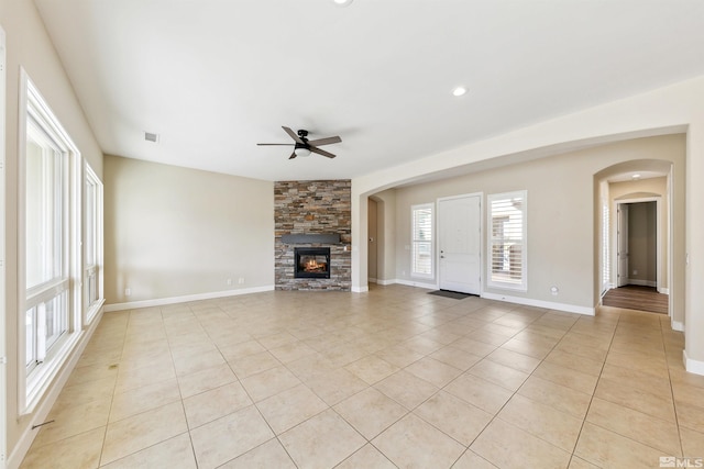 unfurnished living room with ceiling fan, a stone fireplace, and light tile patterned floors