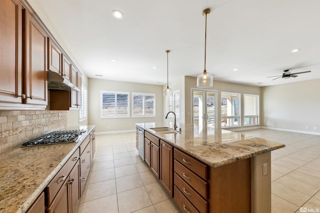 kitchen with sink, light stone counters, pendant lighting, stainless steel appliances, and a kitchen island with sink