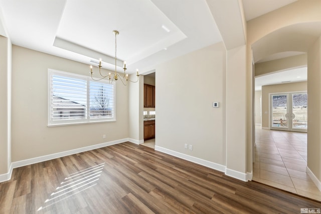 unfurnished dining area with a chandelier, a raised ceiling, and hardwood / wood-style floors