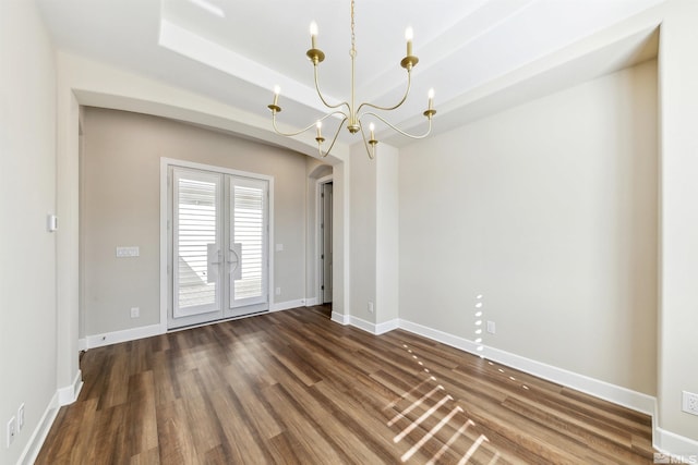 empty room with a notable chandelier, a tray ceiling, dark wood-type flooring, and french doors