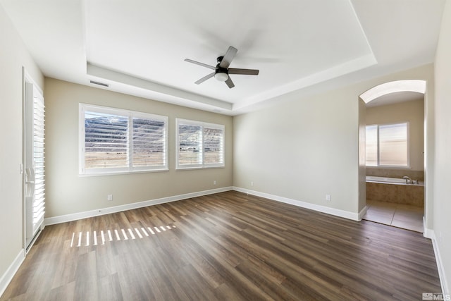 unfurnished bedroom featuring dark hardwood / wood-style floors, connected bathroom, and a tray ceiling