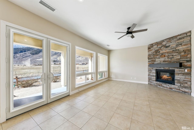 unfurnished living room featuring light tile patterned flooring, a stone fireplace, ceiling fan, and french doors