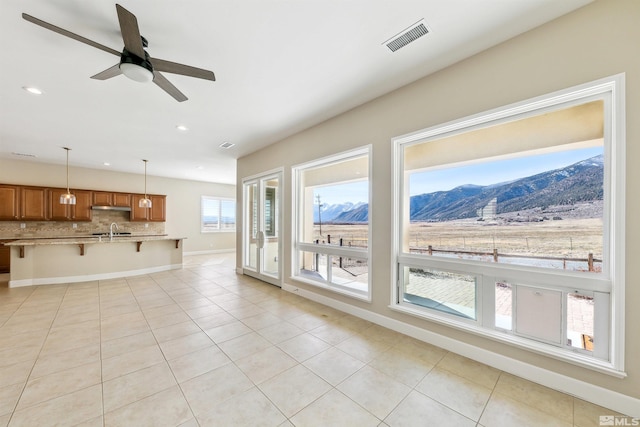 unfurnished living room featuring a mountain view, light tile patterned floors, sink, and ceiling fan