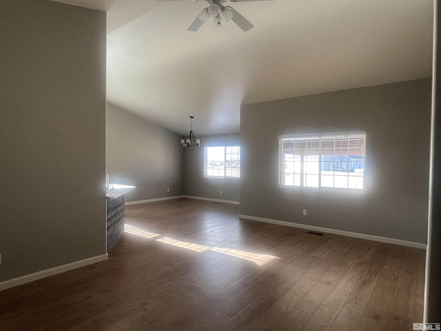 empty room with ceiling fan with notable chandelier, dark hardwood / wood-style flooring, and vaulted ceiling