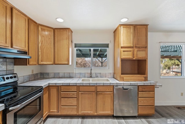 kitchen with wood-type flooring, appliances with stainless steel finishes, sink, and tile countertops