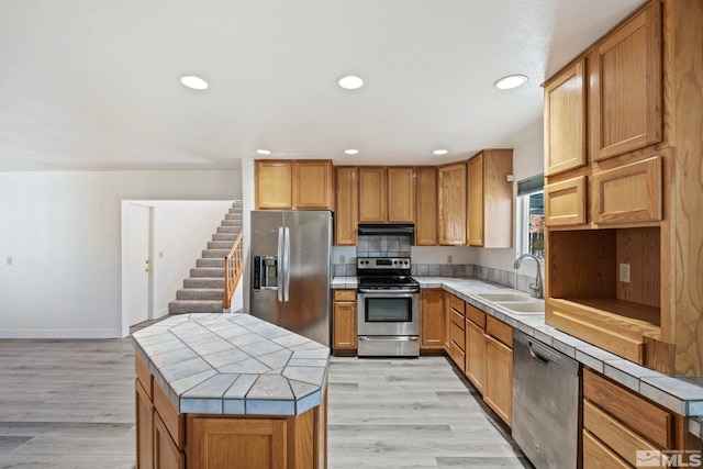 kitchen featuring a kitchen island, appliances with stainless steel finishes, sink, tile counters, and light hardwood / wood-style flooring