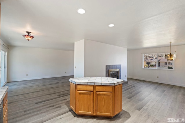 kitchen with decorative light fixtures, a tiled fireplace, a center island, tile counters, and light wood-type flooring