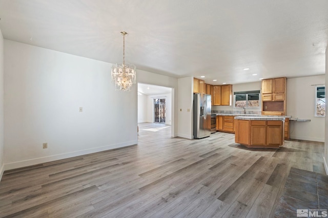 kitchen featuring sink, light hardwood / wood-style flooring, appliances with stainless steel finishes, a kitchen island, and decorative light fixtures