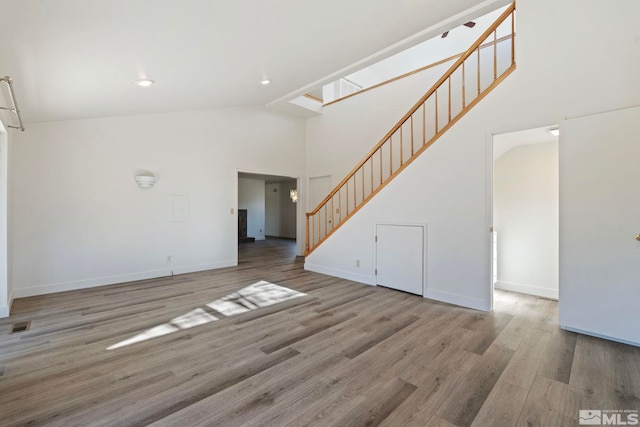 unfurnished living room with wood-type flooring and high vaulted ceiling