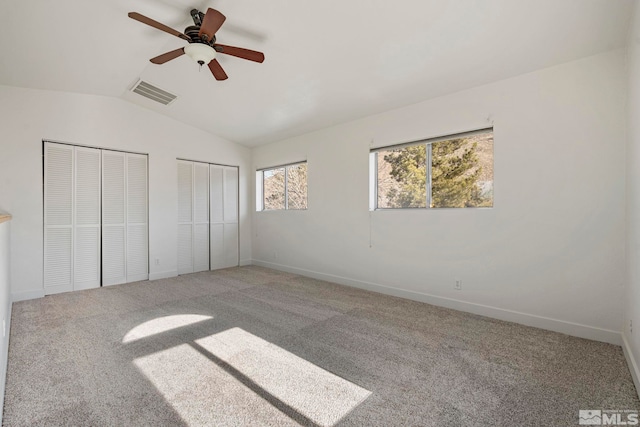 unfurnished bedroom featuring multiple closets, vaulted ceiling, carpet flooring, and ceiling fan