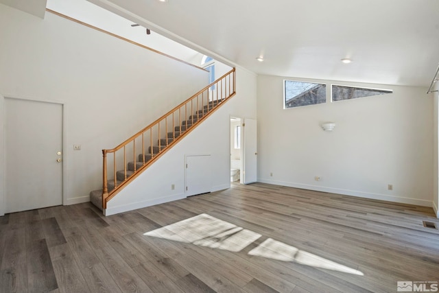 unfurnished living room with a high ceiling and wood-type flooring