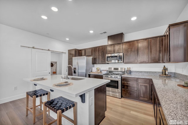 kitchen featuring light wood finished floors, appliances with stainless steel finishes, a barn door, and a sink