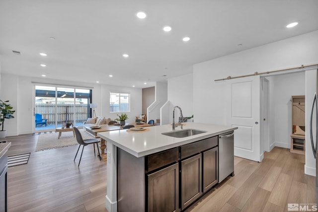 kitchen with a barn door, light wood-style flooring, a sink, and stainless steel dishwasher