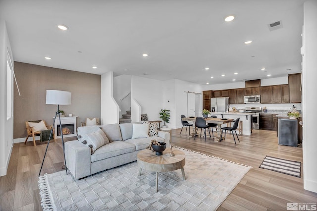 living room featuring stairway, light wood-type flooring, a glass covered fireplace, and recessed lighting