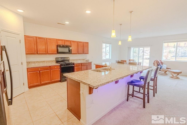 kitchen featuring sink, a breakfast bar area, black appliances, a center island with sink, and decorative light fixtures