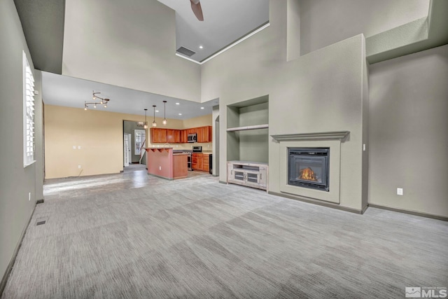 unfurnished living room featuring a high ceiling, light carpet, built in features, and ceiling fan