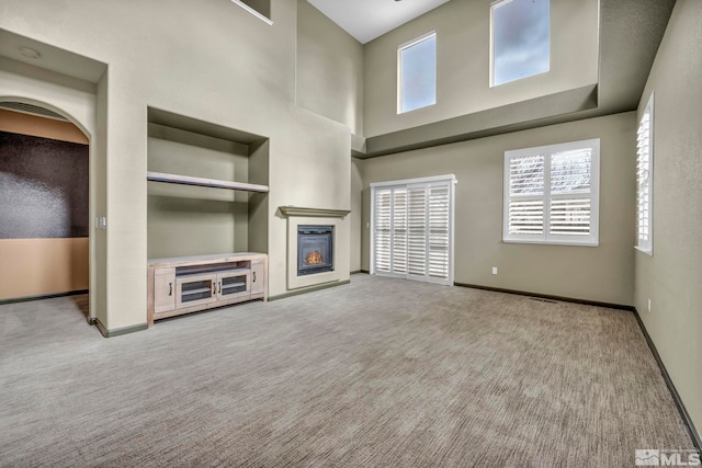 unfurnished living room featuring light colored carpet, plenty of natural light, and a towering ceiling