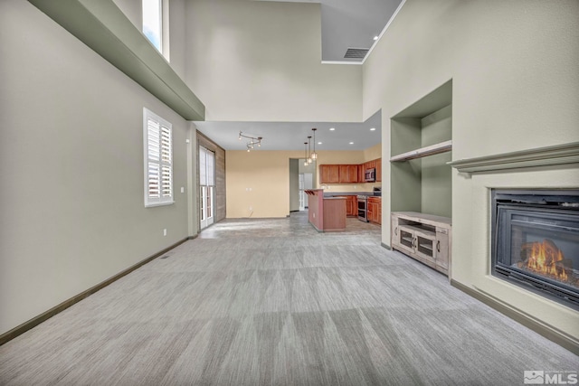 unfurnished living room featuring a towering ceiling, track lighting, and light carpet