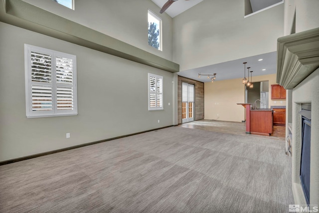 unfurnished living room featuring a towering ceiling, plenty of natural light, and light colored carpet