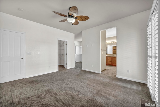 unfurnished bedroom featuring a spacious closet, ceiling fan, dark carpet, ensuite bath, and a closet