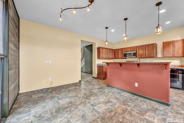 kitchen featuring pendant lighting, a kitchen island with sink, a breakfast bar area, and beverage cooler