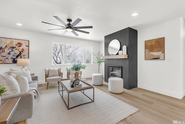 living room with ceiling fan, a large fireplace, and light wood-type flooring