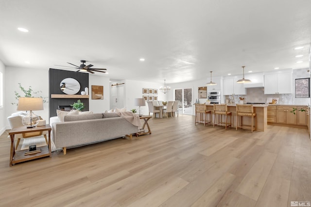 living room featuring ceiling fan with notable chandelier, a large fireplace, and light wood-type flooring