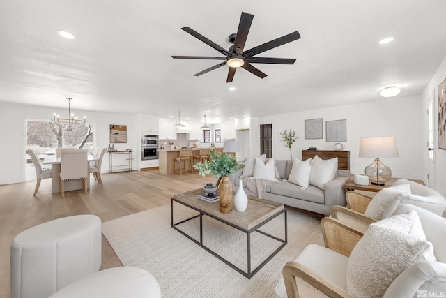 living room featuring ceiling fan with notable chandelier and light wood-type flooring