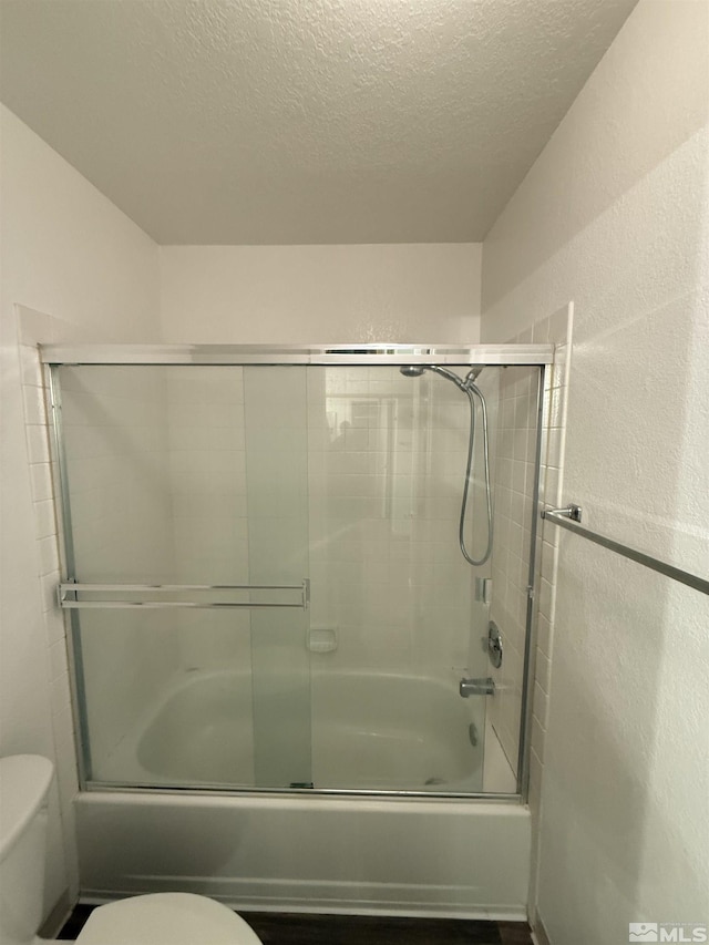 bathroom featuring a textured ceiling, shower / bath combination with glass door, and toilet