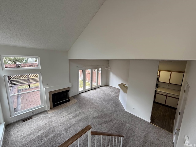 unfurnished living room featuring a tile fireplace, high vaulted ceiling, carpet, and a textured ceiling