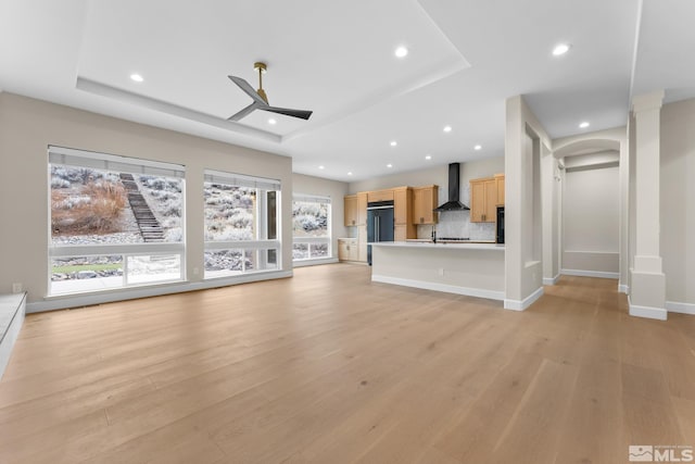 unfurnished living room with a tray ceiling, ceiling fan, and light wood-type flooring