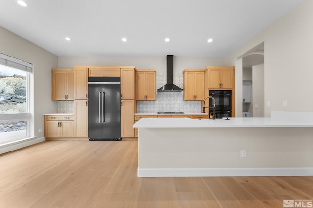 kitchen with decorative backsplash, wall chimney exhaust hood, black appliances, light brown cabinets, and light hardwood / wood-style flooring